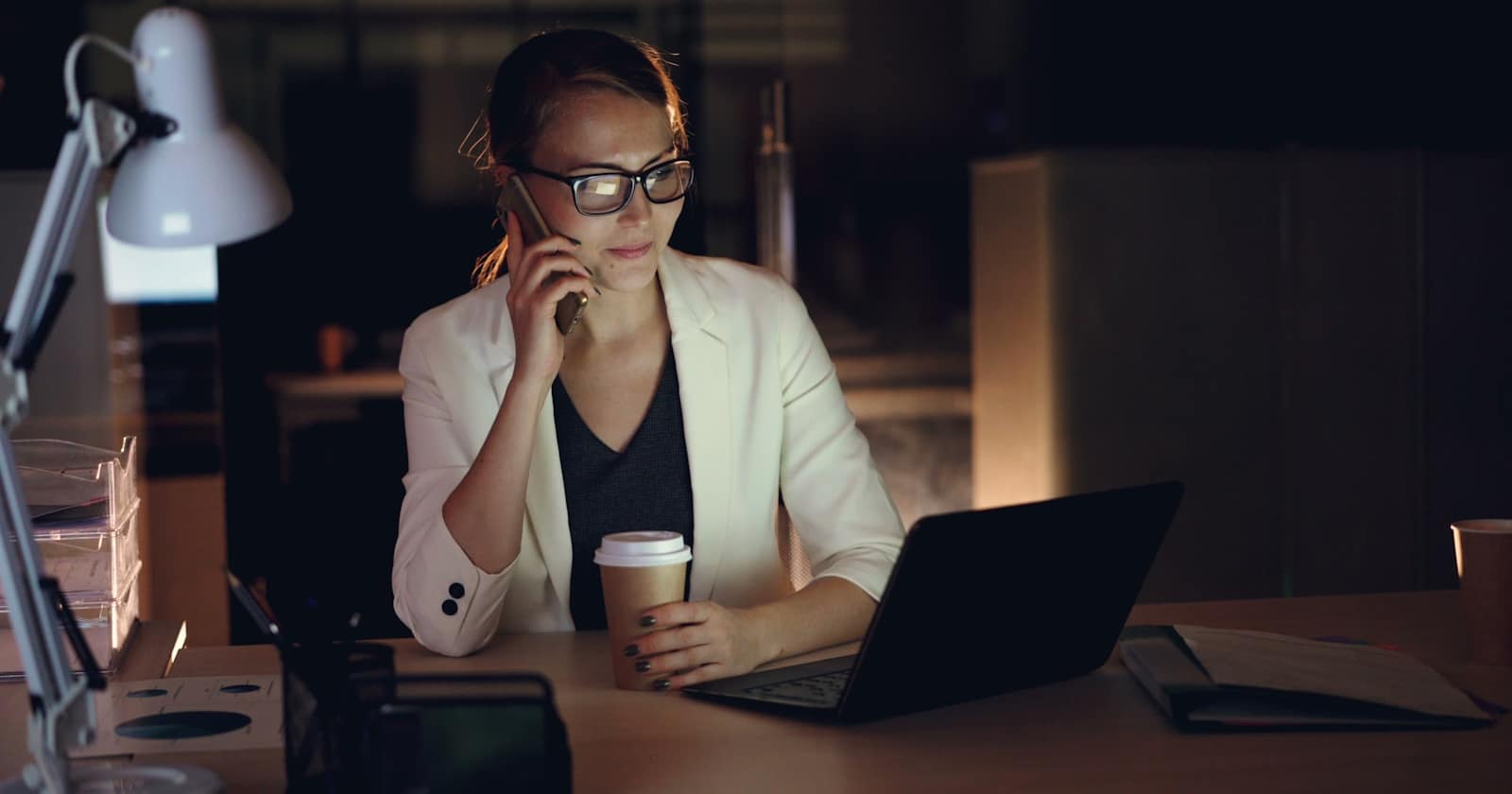 A business owner working late at a desk with a laptop and a phone
