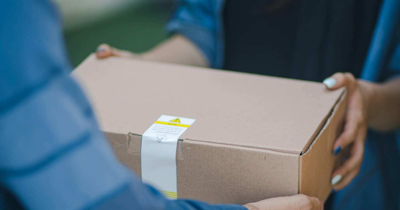 A courier handing a parcel to a customer who is checking a delivery update on their phone.
