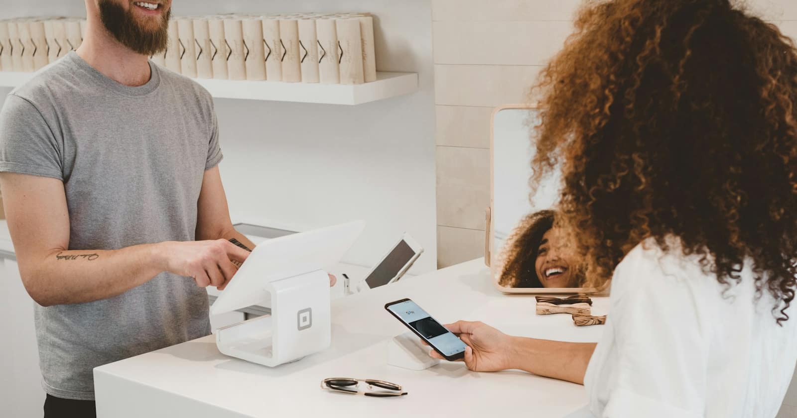 A shop owner wrapping a product at the counter while suggesting a matching item to a customer.