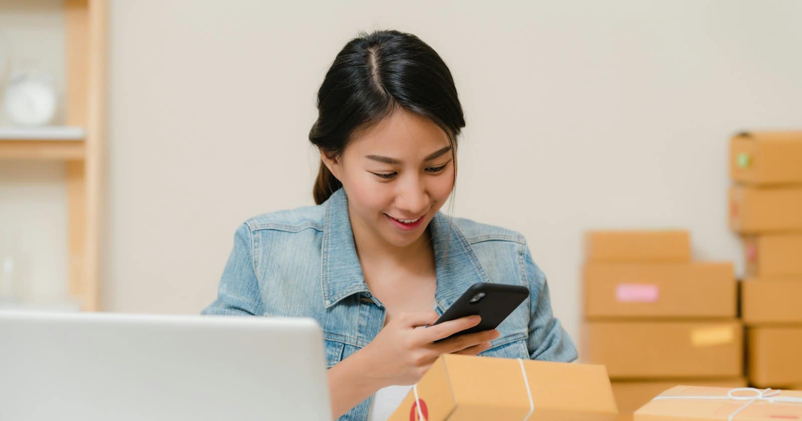 A shop owner packing an order while checking customer messages on a phone
