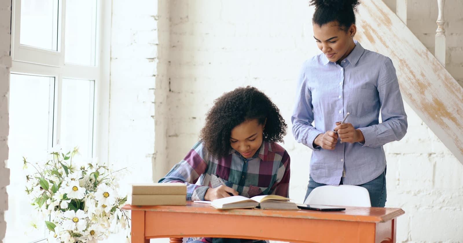 A tutor working through an exercise with a student at a table, notes and a laptop between them.