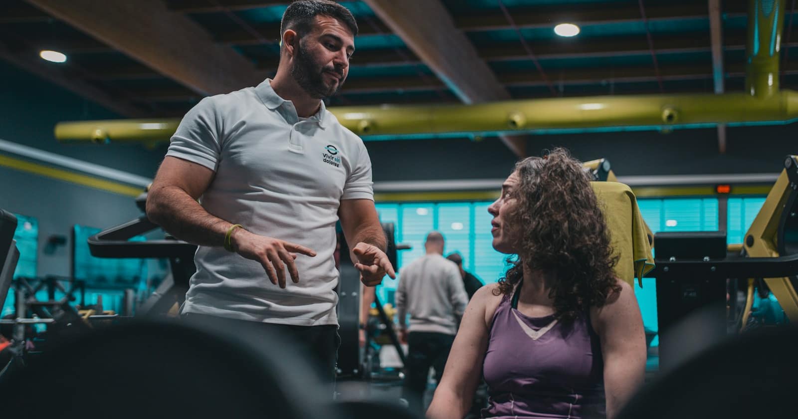 Members training in a bright gym studio while a coach checks the class schedule on a phone.