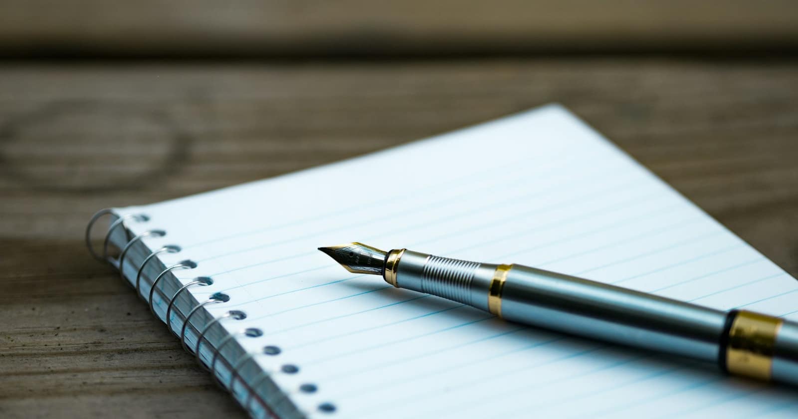 A notebook and pen on a wooden desk beside a window